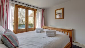A bedroom with a large bed, a wooden headboard, a mirror, and a window with curtains. - Riding Stable - sleeps 6 guests  in 3 bedrooms (Holt)