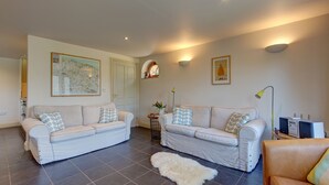 A living room with two white sofas, a white furry rug, and a brown leather chair. - Riding Stable - sleeps 6 guests  in 3 bedrooms (Holt)