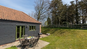 A house with a patio area featuring a table and chairs, a barbecue grill, and a green door. - Wash House - sleeps 6 guests  in 3 bedrooms (Holt)