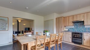 A modern kitchen with wooden cabinets, a tiled backsplash, and a dining area with a wooden table and chairs. - Wash House - sleeps 6 guests  in 3 bedrooms (Holt)