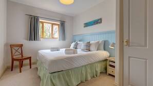 A bedroom with a bed, a chair, a nightstand, a lamp, a window with curtains, and a wall painting. - Wash House - sleeps 6 guests  in 3 bedrooms (Holt)
