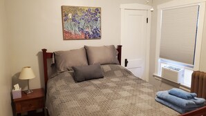 A neatly made bed with a quilt, a bedside lamp, a small bedside table with a tissue box, and a window with blinds. - Updated Forest Park 3 BR Bungalow (Forest Park)