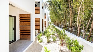 A modern building with a clean, white exterior, wooden slats on the facade, and a narrow pathway lined with small plants and trees. - Seascape Grace Bay Hotel & Townhome Villas (Providenciales)