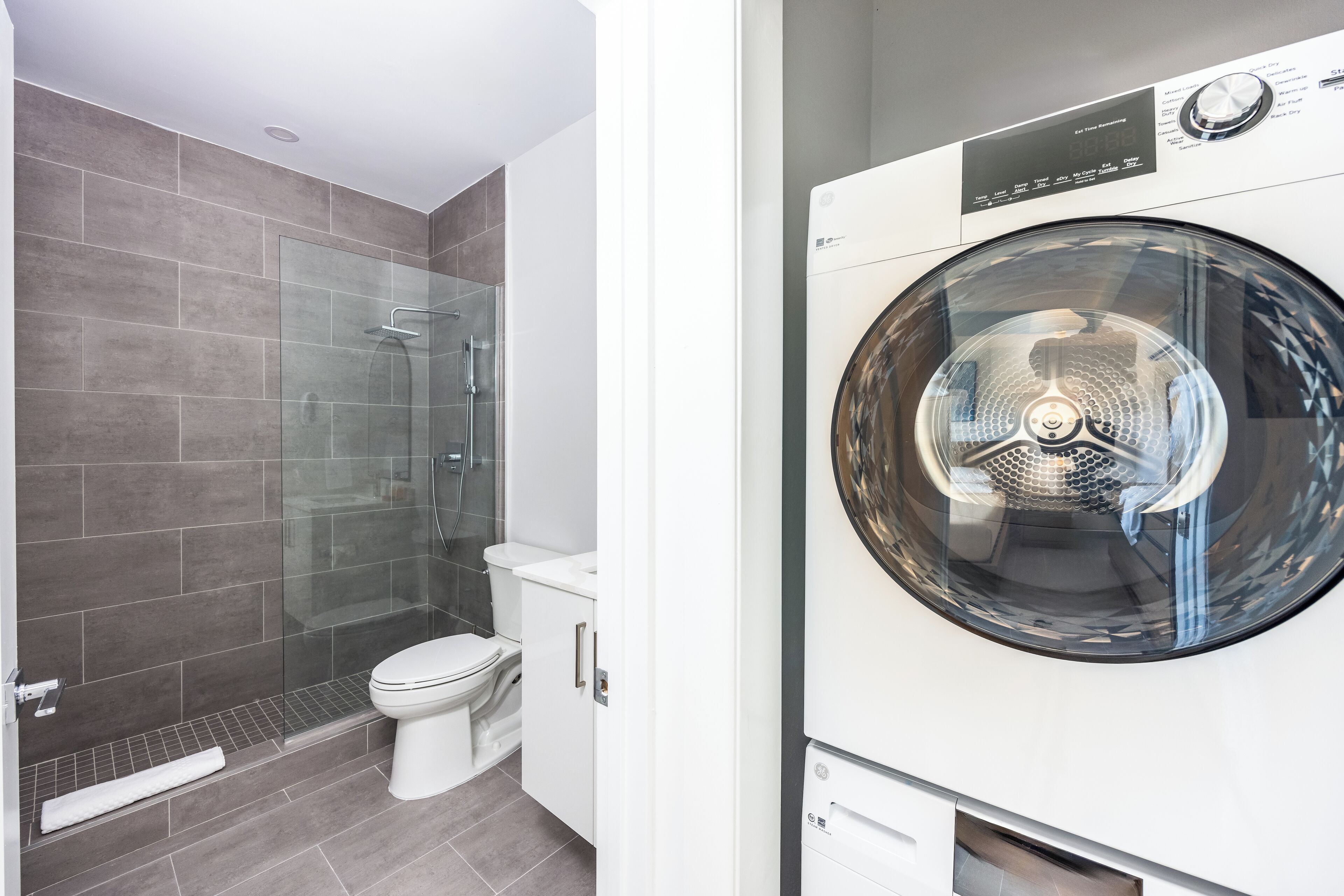 A modern bathroom with a glass shower enclosure, a toilet, and a front-loading washing machine.