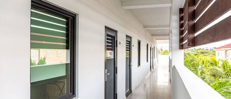 Un pasillo con puertas y ventanas que conduce a un balcón con vistas al follaje.
