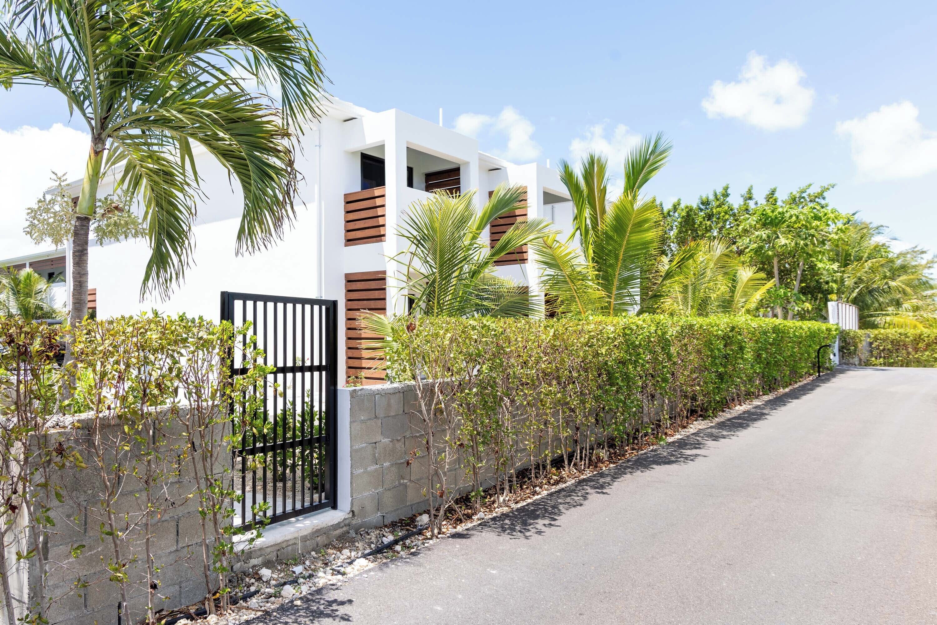 A modern building with a gated entrance, surrounded by well-maintained hedges and palm trees.