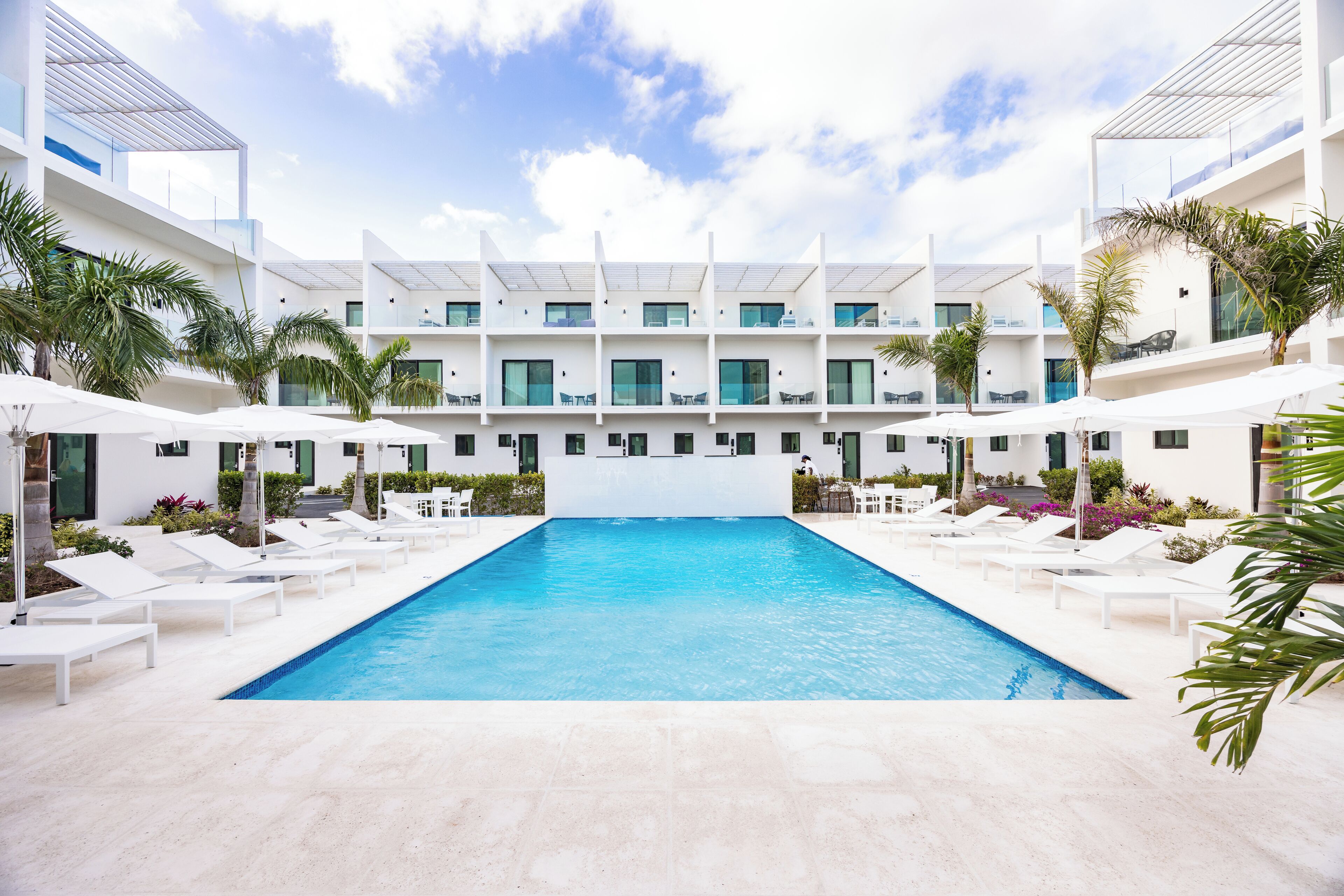 Un hotel moderno con piscina central, varios balcones y zonas de estar al aire libre.