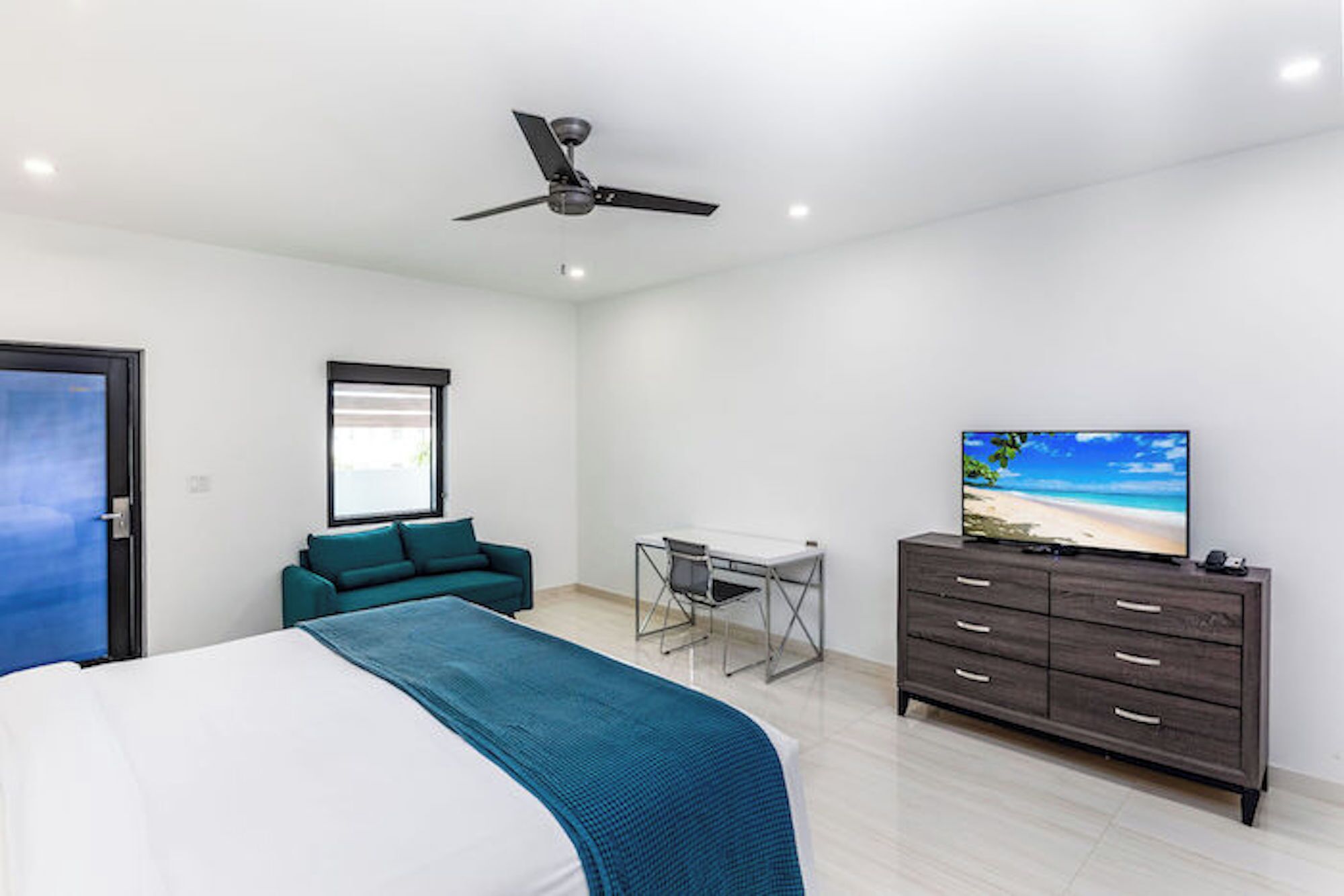 A modern bedroom with a bed, a desk, a chair, a TV, and a ceiling fan.