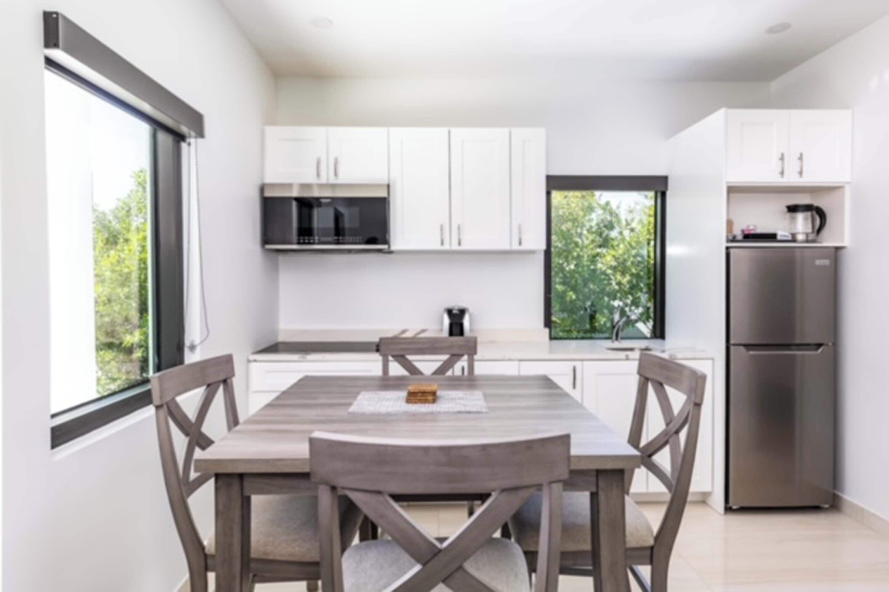 A modern kitchen with white cabinets, a stainless steel refrigerator, and a wooden dining table with chairs.