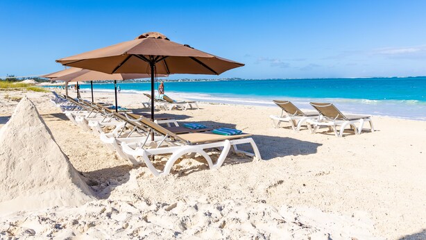 A beach with white lounge chairs and umbrellas, a sandy shore, and a clear blue sea. - Seascape Grace Bay Hotel & Townhome Villas (Providenciales)