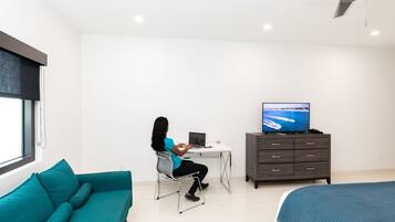 Un dormitorio moderno con un sofá azul aguamarina, un escritorio con una computadora portátil, un televisor y una cama con una manta azul.