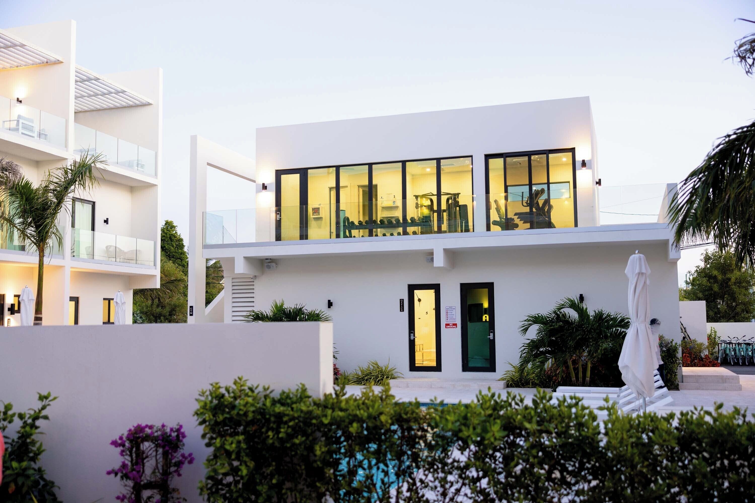 Un edificio moderno de dos pisos con amplios ventanales de vidrio, una escalera y un área de piscina.