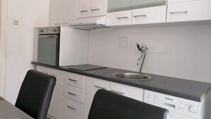 Eine moderne Küche mit weißen Schränken, einer Edelstahl-Spüle, einem eingebauten Backofen und einem Geschirrspüler von Koncar.