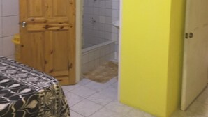 Una habitación con puerta de madera, zona de ducha y cama con colcha estampada.