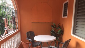 A small balcony with a white round table and four chairs, surrounded by orange walls and a window with blinds. -  Rockery Villa is a cozy 1 Bedroom Townhouse an ideal space for a  getaway. (Port Antonio)