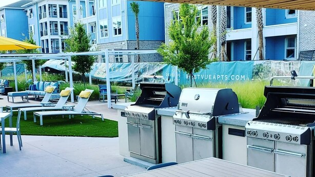 Un espace extérieur aménagé avec un coin barbecue, des chaises longues et une table avec des chaises.