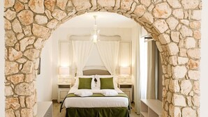 A bedroom with a stone archway, a bed with green bedding, white curtains, and bedside lamps. - Suites La Posada de Pilar (Córdoba)