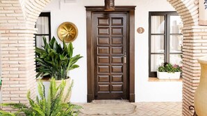A brick archway leading to a wooden door with a brass door knocker, potted plants, and a window with a view of buildings. - Suites La Posada de Pilar (Córdoba)