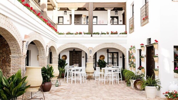 A courtyard with white tiled flooring, white chairs, and potted plants. - Suites La Posada de Pilar (Córdoba)