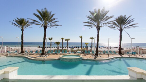 A pool area with palm trees, lounge chairs, and a view of the beach. - Beachfront Family Condo. Luxury Resort. Sleeps 4-6 (Panama City Beach)