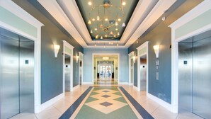 A modern hotel lobby with a central geometric patterned carpet, a ceiling with hanging lights, and elevator doors on either side. - Beachfront Family Condo. Luxury Resort. Sleeps 4-6 (Panama City Beach)