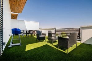 Terraza en la azotea con césped artificial, mobiliario exterior y una parrilla de barbacoa.