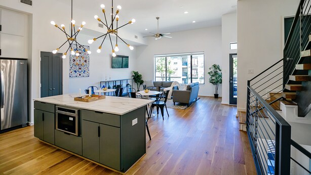 A modern kitchen with a central island, a dining area with a table and chairs, and a staircase with a railing. - Buffalo Heights (Houston)