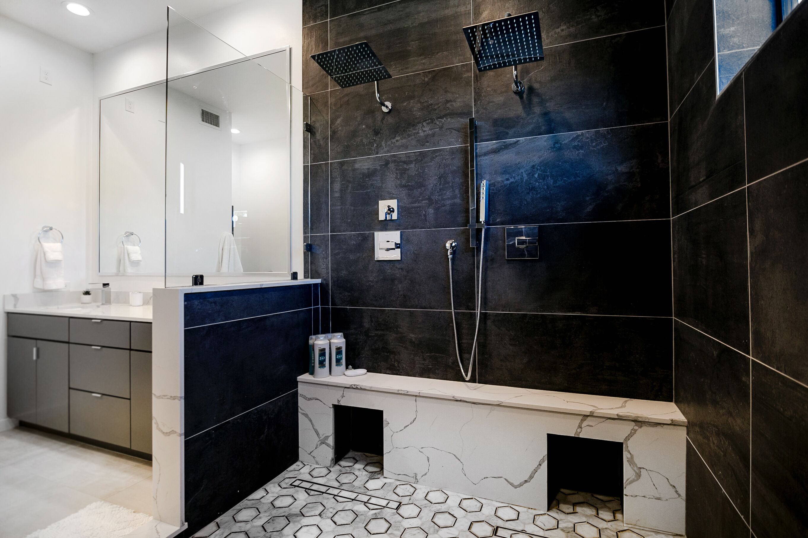 A modern bathroom with dark tiled walls, a glass shower enclosure, and a marble vanity.