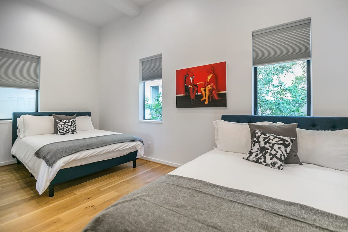 A modern bedroom with two beds, a large window, and a painting on the wall.