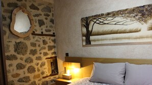 Une chambre avec un mur en pierre, un lit avec des coussins à rayures, une table de chevet avec une lampe et un tableau représentant un arbre.