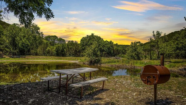 Un coin pique-nique aménagé avec un barbecue et des bancs au bord d’un lac.