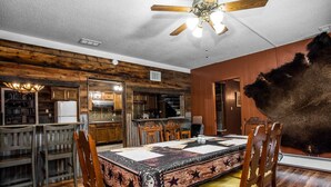 Une salle à manger rustique avec une table et des chaises en bois, un ventilateur de plafond et un mur recouvert de fourrure.