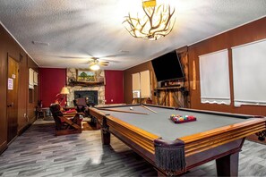 A pool table with a fireplace, a television, and a billiards setup in a room with wooden walls and a herringbone floor pattern. - 3H Ranch Mountain Retreat | 60-Acre Ranch (Medina)