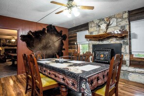 A dining area with a large fur rug, wooden chairs, a stone fireplace, and a ceiling fan.