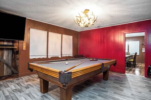 A pool table in a room with wooden flooring, a red wall, and a ceiling light fixture.