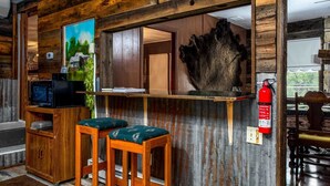 Un coin bar rustique avec des tabourets en bois, un extincteur et un tableau représentant un paysage.
