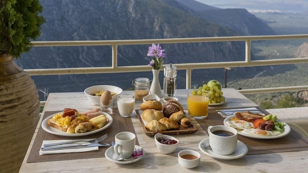 A breakfast table with various dishes and drinks, set against a mountainous backdrop. - Kastalia Hotel (Delphi)