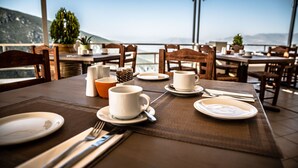 A dining table set with plates, cups, and cutlery, overlooking a scenic view. - Kastalia Hotel (Delphi)