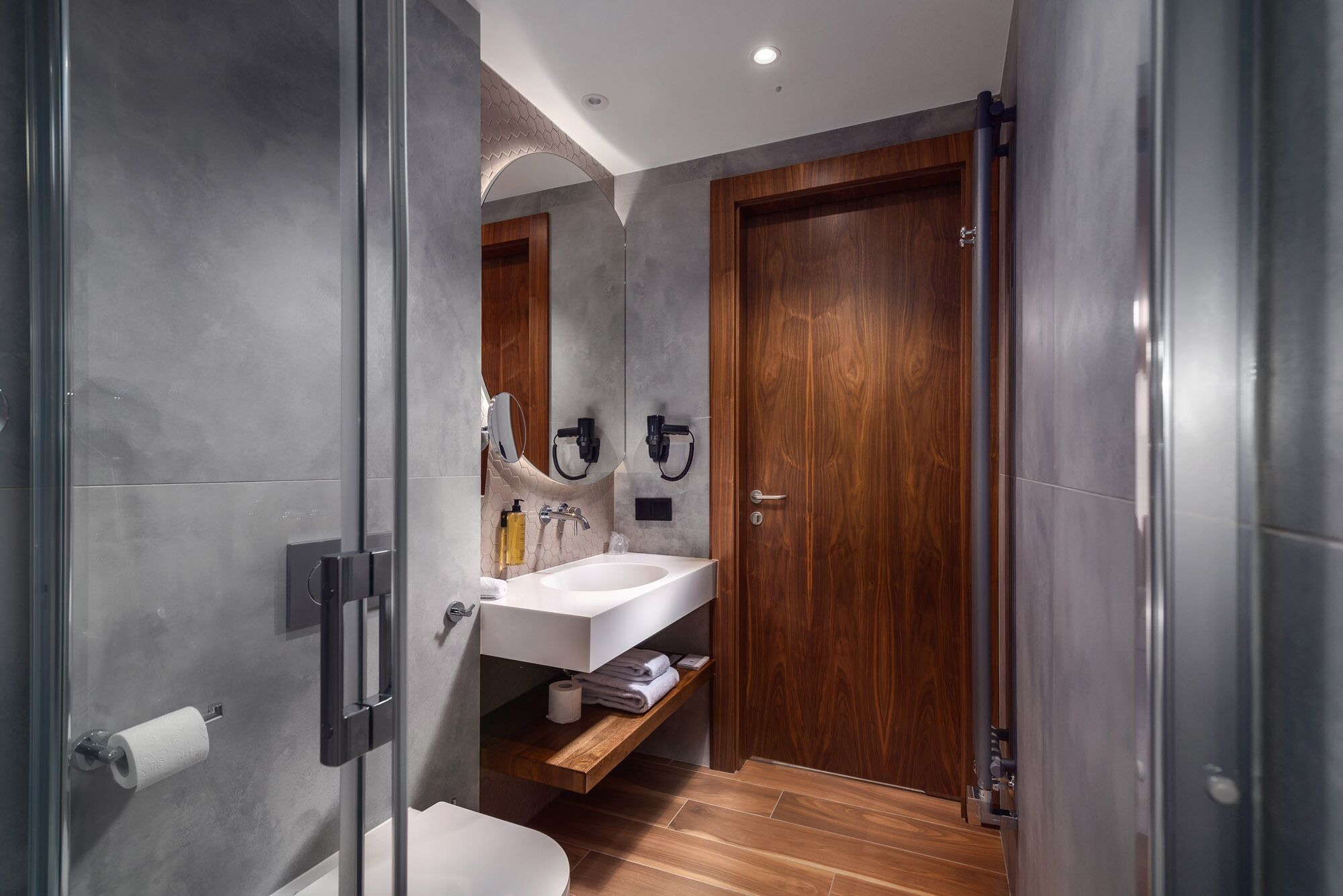 A modern bathroom with a wooden door, a white sink, and a mirror.