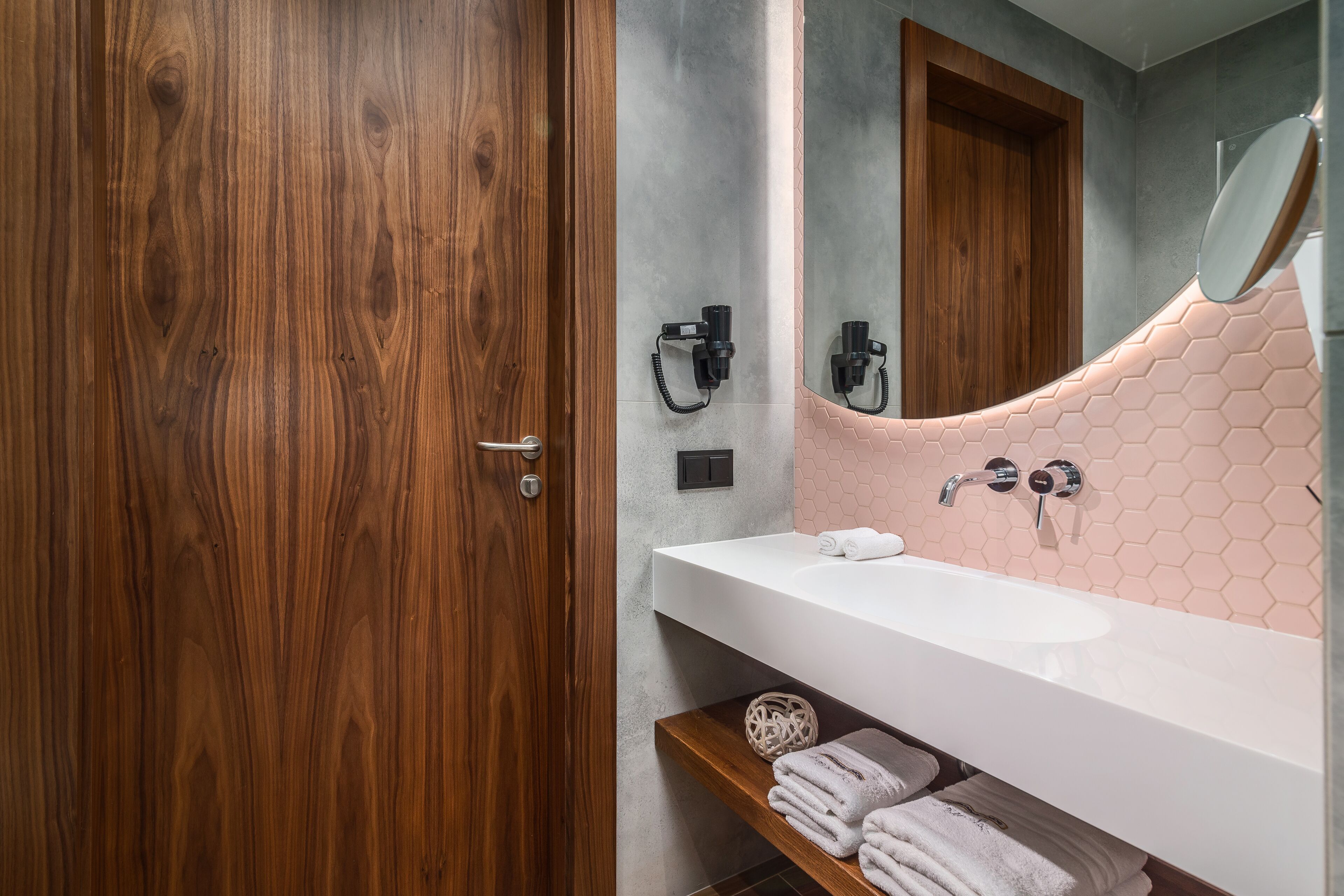 Un baño con puerta de madera, un lavabo blanco, un espejo y un estante para toallas.