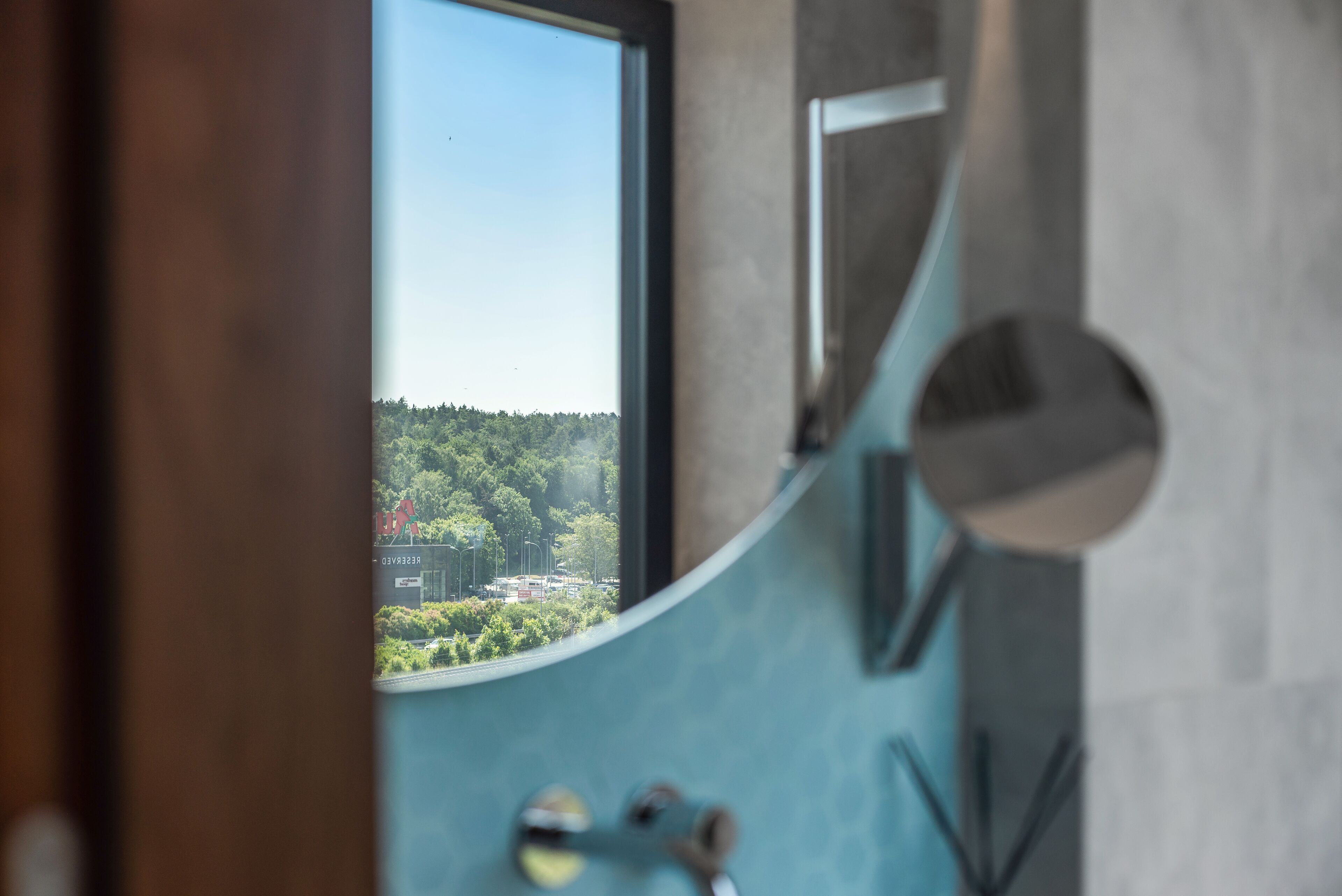 Un baño con un espejo curvo, una ventana y vistas a zona boscosa.