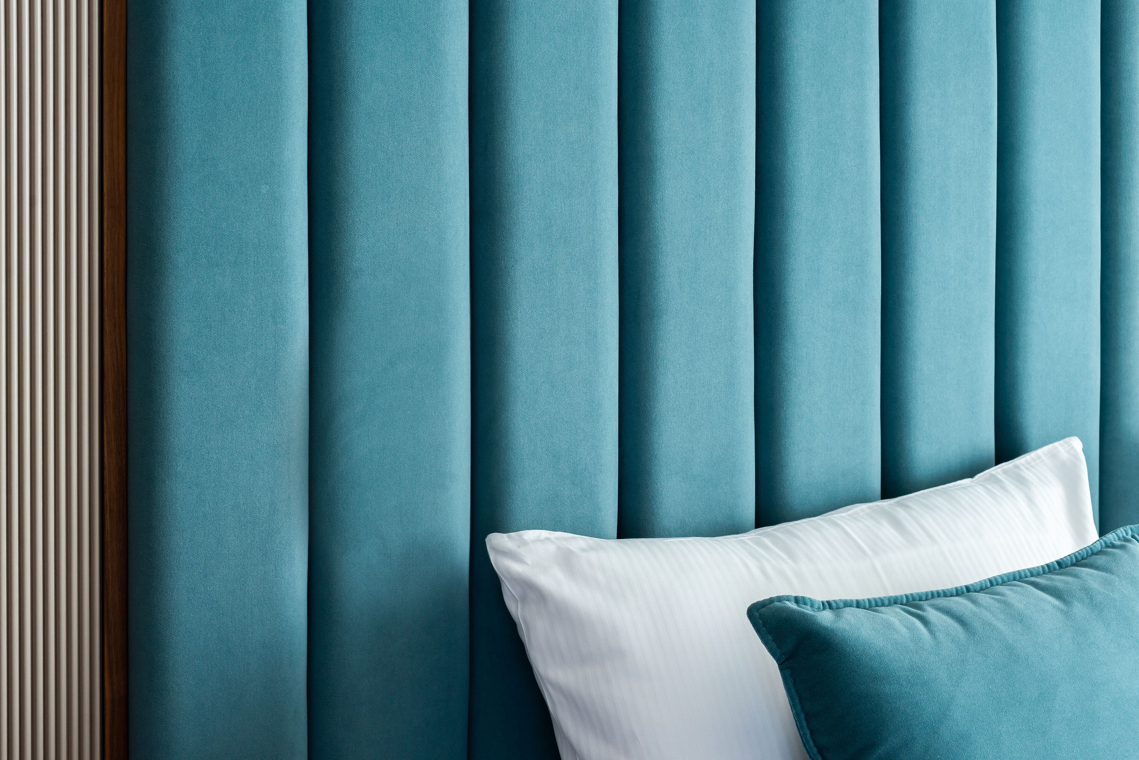 A teal upholstered headboard with vertical slats and a white pillow.