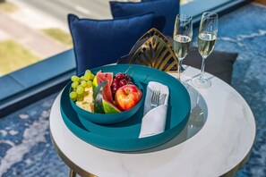 Ett bord med en turkosfärgad skål fylld med frukt, två champagneglas och en vikt servett.