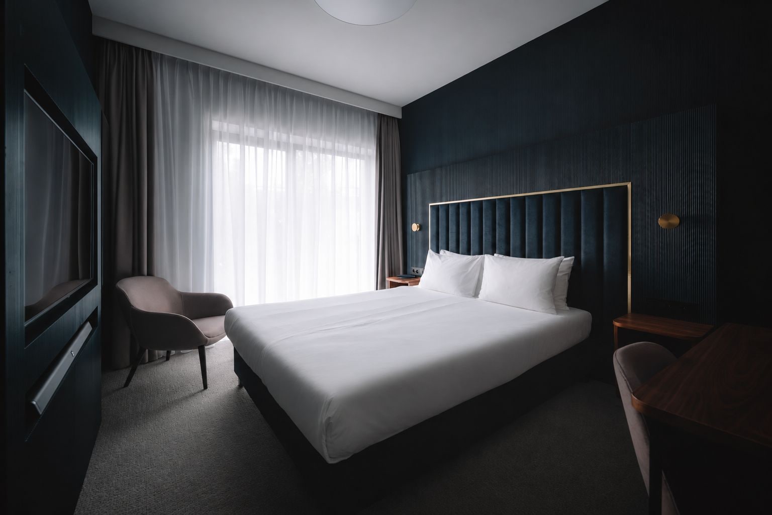 A hotel room with a large bed, a desk, a chair, and a TV.