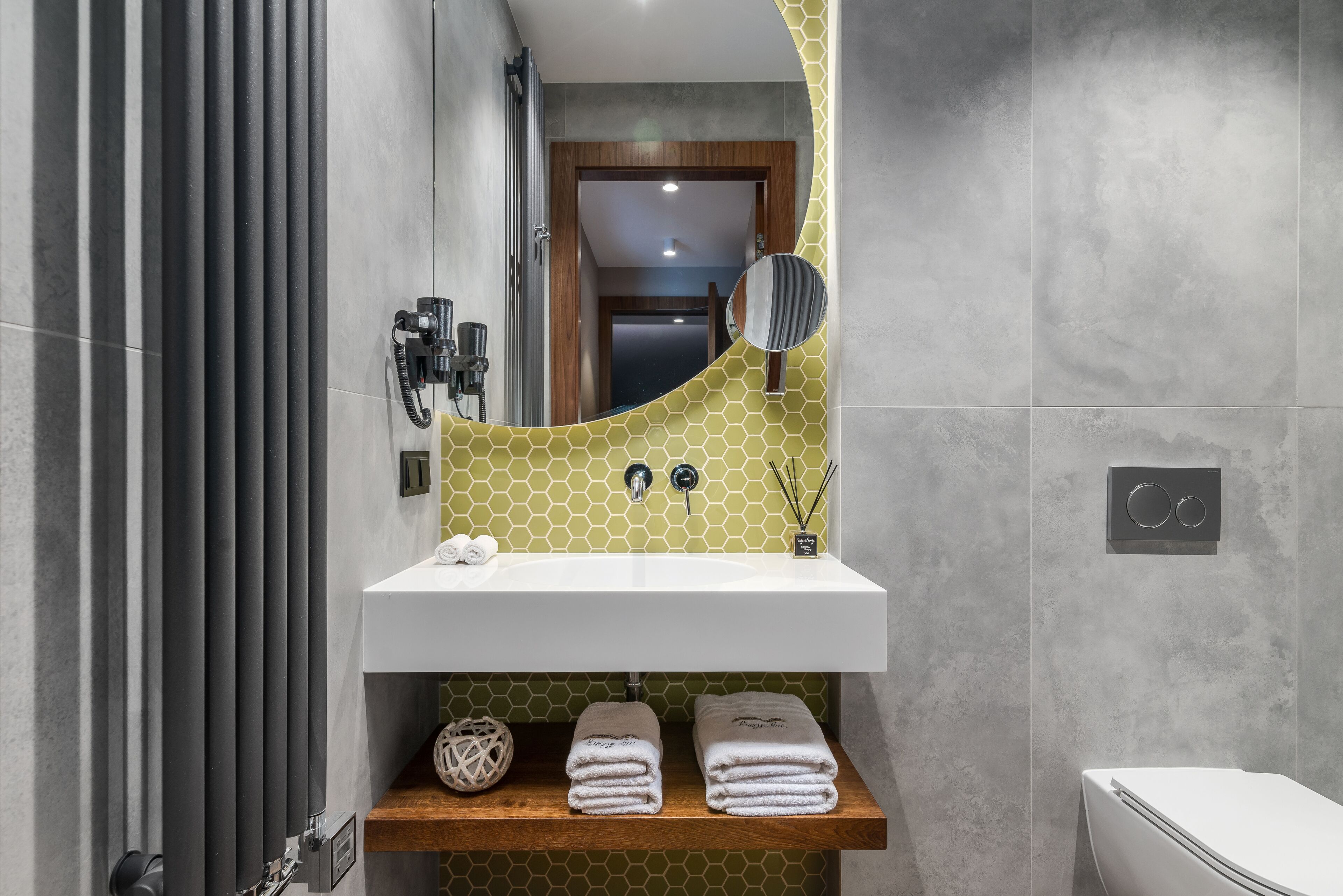 A bathroom with a white sink, a mirror, and a wooden shelf with towels.