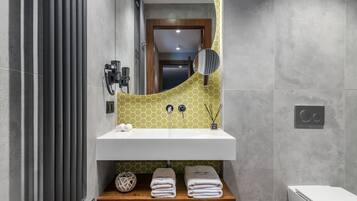 A bathroom with a white sink, a mirror, and a wooden shelf with towels.