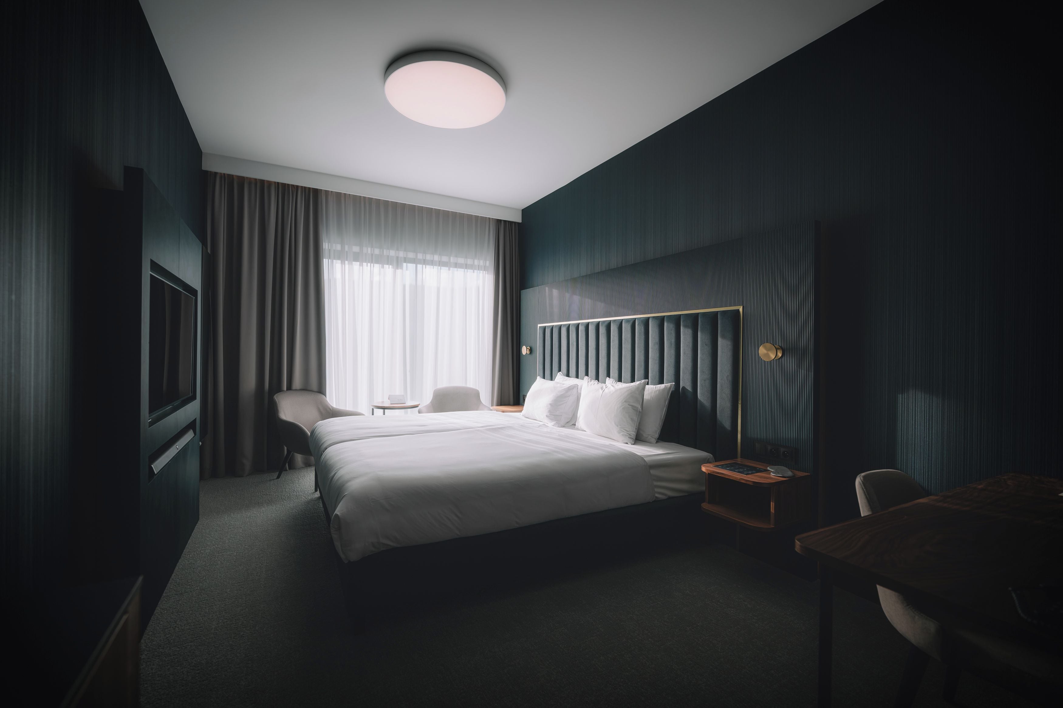 A hotel room with a large bed, a desk, a chair, a TV, and a window with curtains.