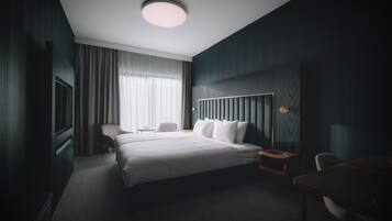 Una habitación de hotel con una cama grande, un escritorio, una silla, un televisor y una ventana con cortinas.