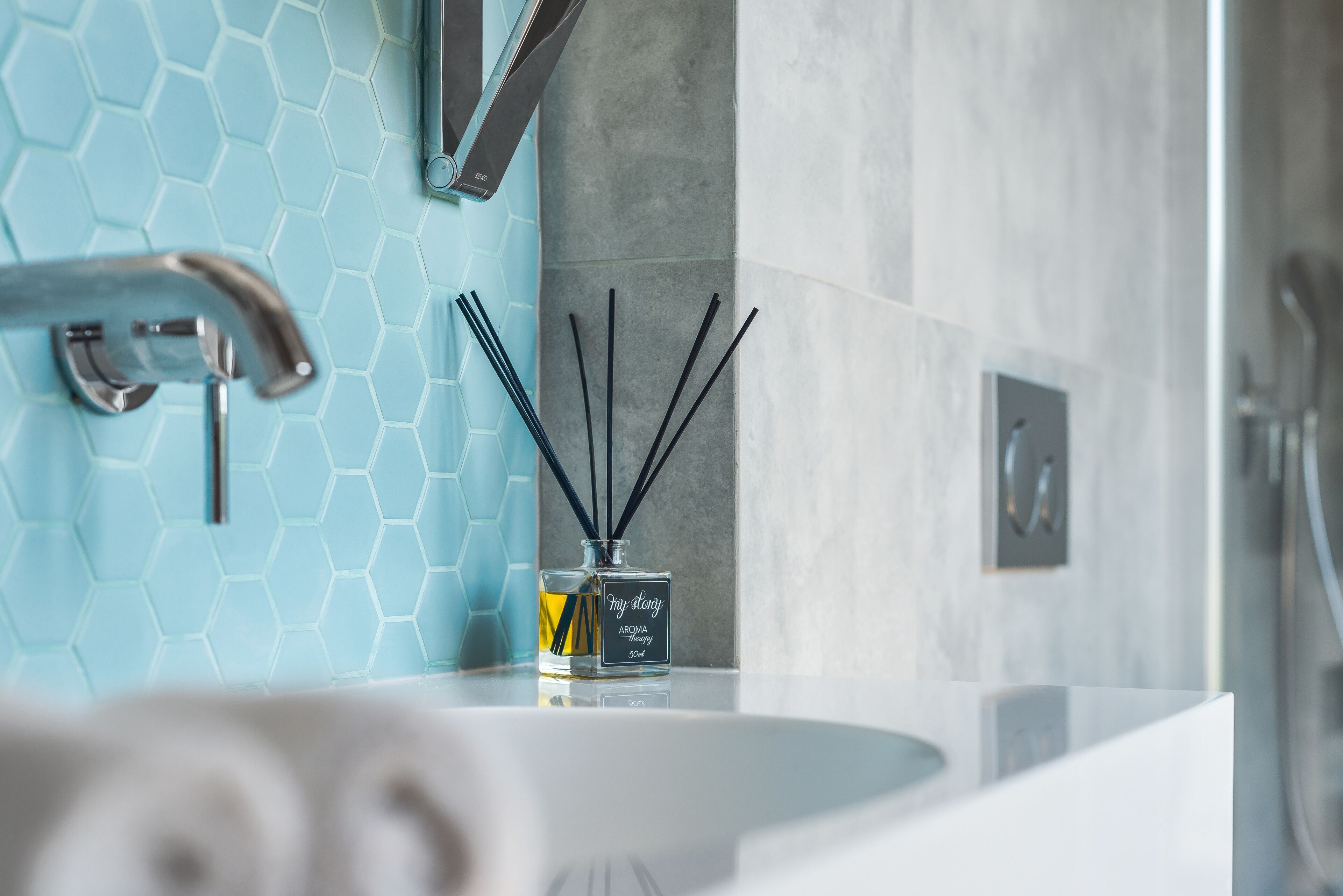 Un baño con diseño moderno, que incluye un lavabo blanco, un recipiente de vidrio con cañas negras y un salpicadero de azulejos hexagonales azules.