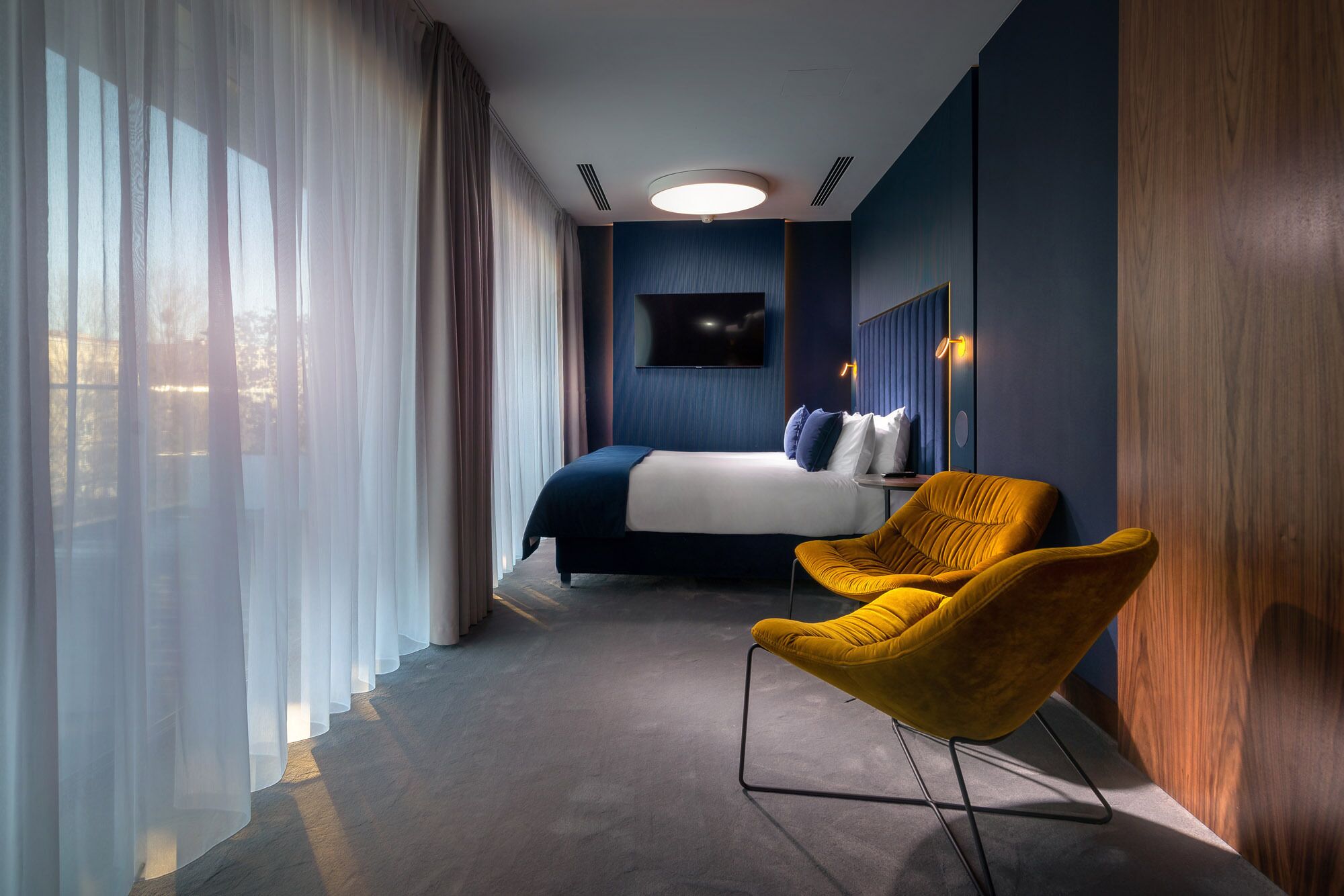 A modern hotel room with a large bed, a television, and a yellow armchair.